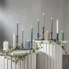 A collection of LED candles of various colors and sizes arranged on white pedestals, decorated with ivy. Podgląd zdjęcia produktu