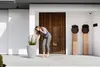 A woman is tending to a large planter in front of a modern house with a slatted wooden door. Náhľad obrázku produktu