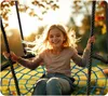 A young girl is happily swinging on a large nest swing outdoors during sunset. Podgląd zdjęcia produktu