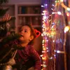 A young child looks up at a decorated Christmas tree, with colorful fairy lights in the background. Náhled obrázku produktu