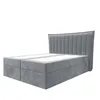 A grey upholstered box spring bed with a fluted headboard, shown from a side-angle against a white background. Produktbild-Vorschau