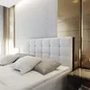 A close-up view of a bed in a modern bedroom, featuring a white tufted headboard, white bedding, and gold accent walls. Produktbild-Vorschau
