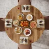 A round wooden dining table set for a meal with various dishes and place settings. Podgląd zdjęcia produktu