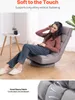 A woman is sitting on a floor chair, wearing headphones and listening to music. The chair is in a living room setting with a small side table and a plant in the background. A close-up of the chair's fabric is shown at the bottom. Voir les images du produit