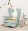 A plush goose toy sits in a light blue armchair next to a floor lamp and small side tables. Podgląd zdjęcia produktu