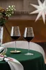 Two wine glasses filled with red wine are placed on a green tablecloth, with festive decorations in the background. Produktbild-Vorschau