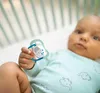 A baby holding a pacifier in a crib. Produktbild-Vorschau