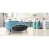 A blue retro-style space heater sits on a countertop next to two blue soap dispensers and a stack of white towels. The background shows a blurred kitchen or bathroom setting. Produktbild-Vorschau
