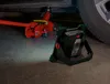 A red car jack and a portable work light are on a concrete floor next to a car tire. Produktbild-Vorschau