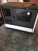 A black and white wood-burning stove with a glass oven door and a thermometer is shown in a room with a concrete floor. Produktbild-Vorschau