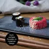 Sushi on a dark gray rectangular plate with chopsticks and decorative flowers in the background. Produktbild-Vorschau