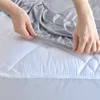 Hands are shown tucking a grey fitted sheet over a white quilted mattress protector. Produktbild-Vorschau