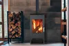 A modern wood-burning stove with a stack of firewood next to it, set against a textured concrete wall. Produktbild-Vorschau