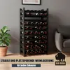 A black wine rack filled with wine bottles, placed in a room with a plant and a sofa. Text overlays describe the product's features. Produktbild-Vorschau