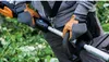 A person wearing gloves is holding a string trimmer in a garden. Produktbild-Vorschau