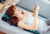 A woman is lying on a couch with an acupressure mat and pillow, using her phone. Náhľad obrázku produktu