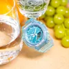 A blue Casio G-Shock watch is placed on a tan surface next to a glass of orange juice and a glass of water with grapes in the background. Produktbild-Vorschau
