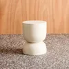 A cream-colored stool or side table is placed on a speckled surface in front of a wooden background. Anteprima dell’immagine prodotto