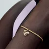 A close-up shot of a person's arm wearing a gold bracelet with a monstera leaf charm. Podgląd zdjęcia produktu