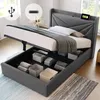 A grey upholstered bed frame with the mattress lifted to reveal storage compartments underneath. A tablet is charging on the headboard. Produktbild-Vorschau
