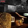 A split image showing a house at night, with the top half unlit and the bottom half illuminated by warm white string lights on the bushes and roofline. Produktbild-Vorschau