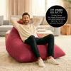 A man is relaxing on a large red beanbag chair in a living room. Voir les images du produit