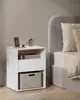 A bedside table with a phone charging, a clock, and books next to a bed. Produktbild-Vorschau