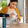 A woman is pouring liquid from a small container into a baby bottle. Anteprima dell’immagine prodotto