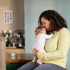 A woman is holding and kissing a baby in a home environment. Produktbild-Vorschau