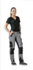 A woman is standing and posing in a studio setting, wearing work pants and a t-shirt. Produktbild-Vorschau