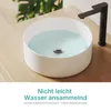 A white ceramic sink filled with water, with a black faucet. The sink is on a wooden surface, with a plant in the background. Produktbild-Vorschau