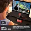 A man is using a treadmill with a large screen displaying an interactive workout. The screen shows a virtual landscape and workout metrics. A phone is charging on a built-in dock. Produktbild-Vorschau