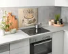 A kitchen counter with a glass backsplash featuring a coffee cup design, a stovetop with a pot, and various kitchen accessories. Produktbild-Vorschau