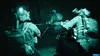Three soldiers in tactical gear moving through a dark, narrow passage, illuminated by headlamps and possibly night vision. Produktbild-Vorschau