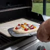 A pizza is being placed on a grill using a pizza peel. Náhled obrázku produktu