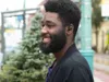 A man wearing earbuds and smiling outdoors. Anteprima dell’immagine prodotto