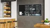 A cafe interior with a menu board on the wall, a counter with stools, and tables. Produktbild-Vorschau