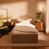 A bedroom scene with a bed, nightstand, chair, and lamp, bathed in warm light. Produktbild-Vorschau