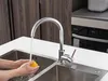 A person is washing a lemon under a faucet in a kitchen sink. Anteprima dell’immagine prodotto