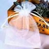 A white organza gift bag is shown in the foreground, with a wooden crate containing succulents in the background. Produktbild-Vorschau