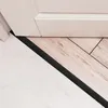 A close-up view of a transition strip between two different flooring types, with a baseboard visible above. Podgląd zdjęcia produktu