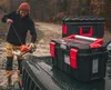 A man is preparing a chainsaw next to two toolboxes on the back of a vehicle. Anteprima dell’immagine prodotto