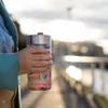 A person holding a floral-patterned Quokka Boost thermal mug outdoors during sunset. Anteprima dell’immagine prodotto