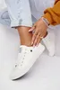 A person wearing white sneakers and jeans, with jewelry on their hand. Podgląd zdjęcia produktu