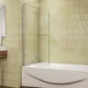 A shower screen attached to a bathtub in a bathroom with tiled walls. Produktbild-Vorschau