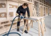 A man is using a circular saw on a piece of wood supported by sawhorses in a construction setting. Produktbild-Vorschau