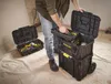 A person is organizing tools in a modular toolbox system on wheels in what appears to be a construction or renovation site. Voir les images du produit