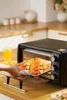 A hand places a baking tray with food into a mini oven in a kitchen. Náhľad obrázku produktu
