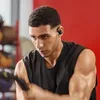 A man is working out in a gym, wearing black earbuds. Produktbild-Vorschau