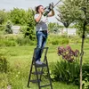 A man is using a hedge trimmer while standing on a ladder in a garden. Náhled obrázku produktu